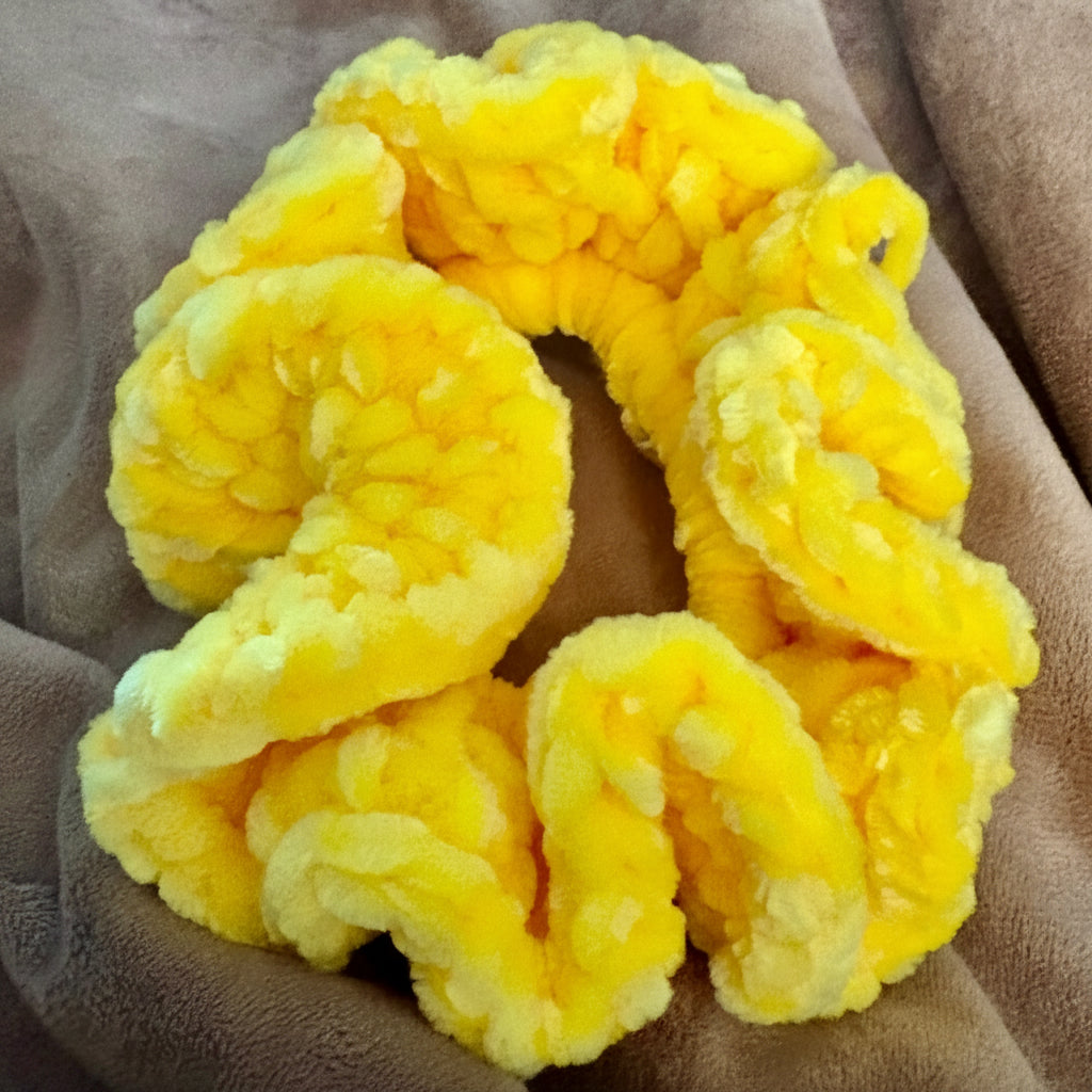 A bright yellow, highly textured and bubbly scrunchie made of plush, fuzzy fabric, resting on a brown fleece blanket.