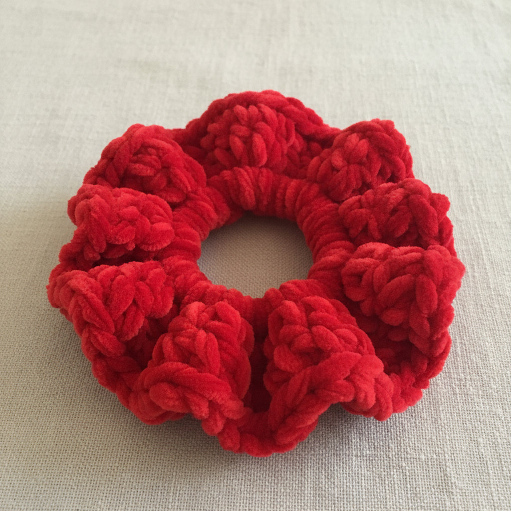A bright red textured faux fur or plush scrunchie resting on a soft gray blanket.