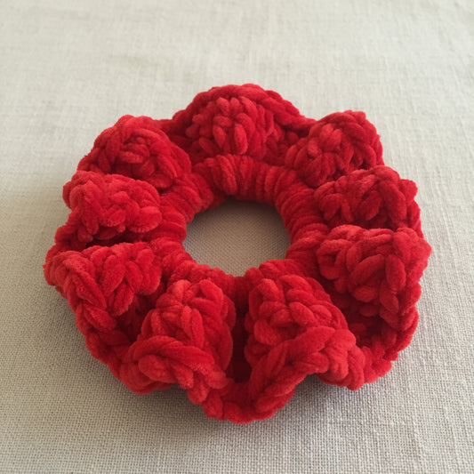 A bright red textured faux fur or plush scrunchie resting on a soft gray blanket.